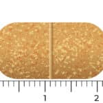 A tan, speckled oblong tablet of Vitakruid – Multi Day & Night® Mama (2 x 30 Tablets) with a scored center is shown next to a ruler, measuring about 2 cm long and 1 cm wide.